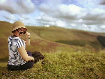 Rear view portrait of woman sitting on grassy field against cloudy sky