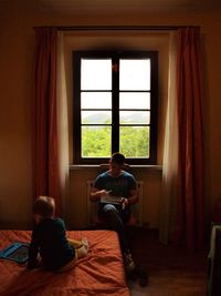 Father using laptop while son playing on bed at home