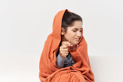 Young woman looking away while sitting against white background