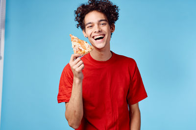 Portrait of smiling young man eating ice cream against blue sky