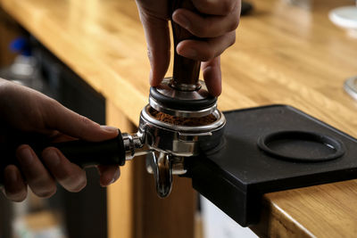 Cropped hands crushing coffee beans in portafilter at cafe