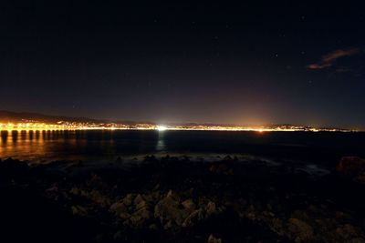 Illuminated city by sea against sky at night