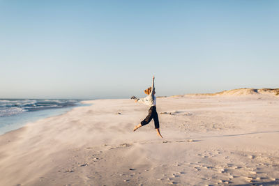 Young woman jumping at beach against clear sky during sunset