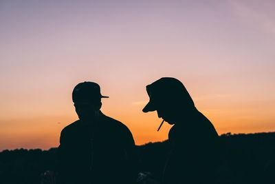 Silhouette of men smoking cigarette against sky during sunset