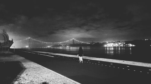 Illuminated suspension bridge over river against sky