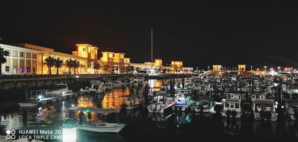 Illuminated buildings by river against sky in city at night