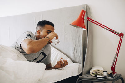 Man taking pills while lying on bed by side table at home