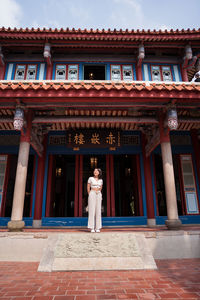 Full body of young asian female traveler in stylish outfit looking away while standing near entrance of ancient tainan confucian temple during trip in taiwan