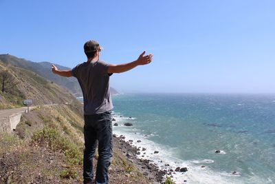 Rear view of man standing by sea against clear sky