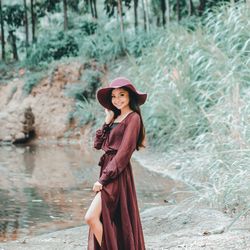 Portrait of young woman in hat standing at lake