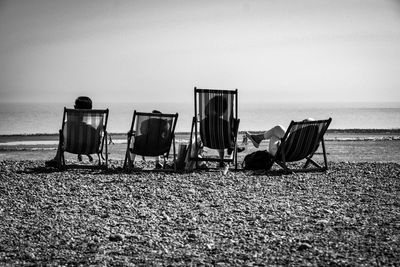 Rear view of friends relaxing on deck chairs at beach against sky