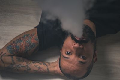 High angle portrait of mid adult man emitting smoke while lying on hardwood floor