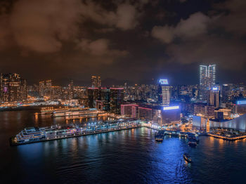 Illuminated buildings by river against sky at night