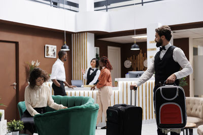 Side view of woman using mobile phone while sitting on suitcase at home