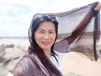 Portrait of smiling woman wearing scarf standing against sky