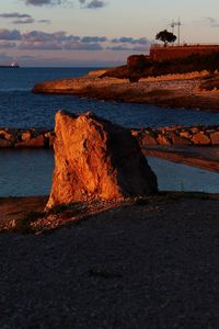 Rock formation on beach against sky during sunset