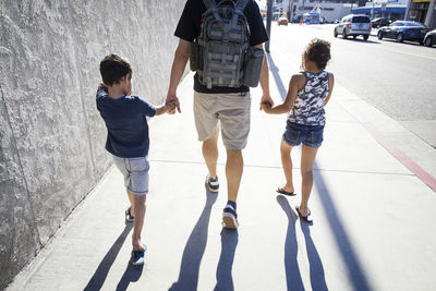 Rear view of father walking with children on sidewalk in city