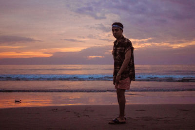 Full length of young man standing on beach against sky during sunset