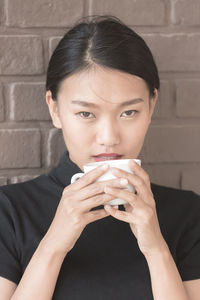 Close-up portrait of a young woman holding drink against wall
