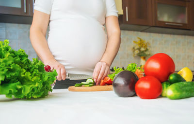 Midsection of pregnant woman cutting vegetable