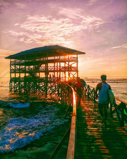 Man on pier by sea against sky during sunset