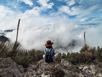 Woman sitting on rock looking at mountain against sky