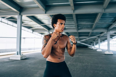 Shirtless male athlete exercising below bridge in city