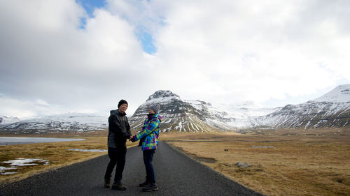 Couple holding hands standing on road against cloudy sky