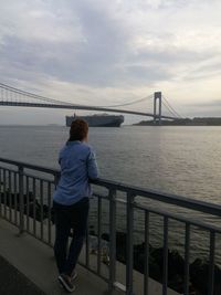 Rear view of man looking at suspension bridge over river