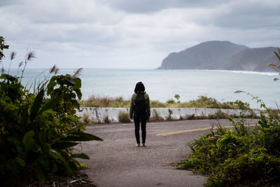 Rear view of woman walking on sea shore against sky