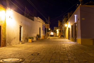 Illuminated street amidst buildings at night