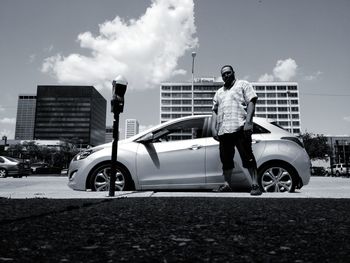 Man standing by car against sky in city