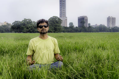 Portrait of man wearing sunglasses meditating while sitting on grassy field