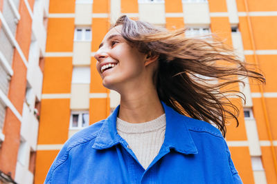 Low angle of cheerful female standing in street against bright building and laughing