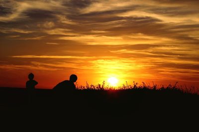 Silhouette people against orange sky during sunset