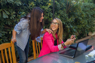Female colleagues using mobile phone against plants