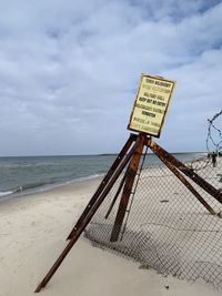 Information sign on beach against sky