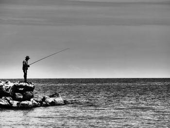 Side view of man fishing while standing rock in sea