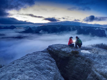 People on rock in mountains against sky