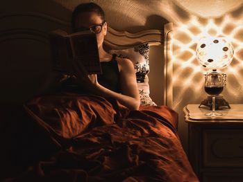 Young woman relaxing reading in bed with glass of wine with nightlight on