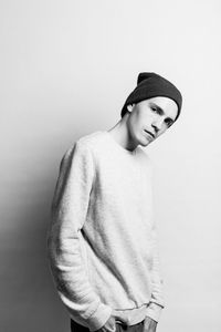 Portrait of young man wearing knit hat standing against white background