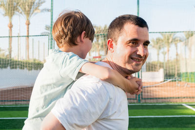 Happy father carrying son on back at sports ground