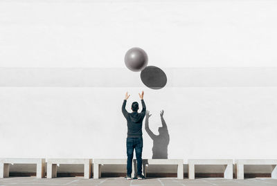 Rear view full length of man playing with ball against wall