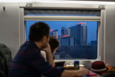 Rear view of man and woman sitting on window