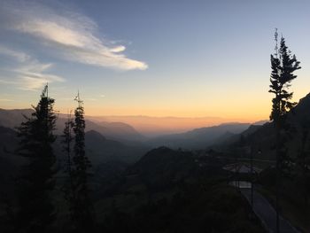 Scenic view of silhouette mountains during foggy weather at sunset