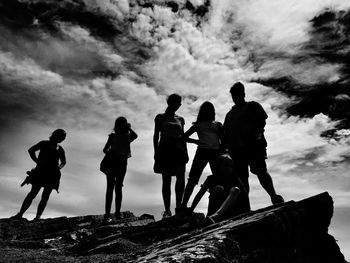 Silhouette of people standing on mountain against cloudy sky