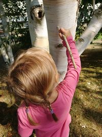 Rear view of girl scratching tree trunk with stick