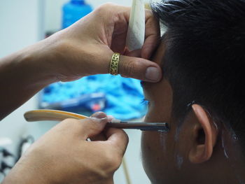 Cropped hands of barber cutting customer beard in salon