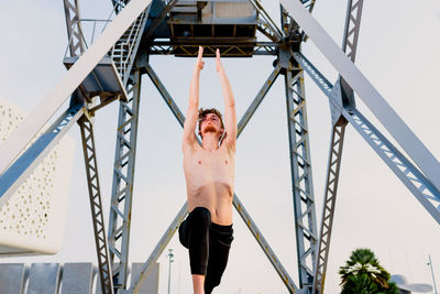 Low angle view of woman standing on railing against sky