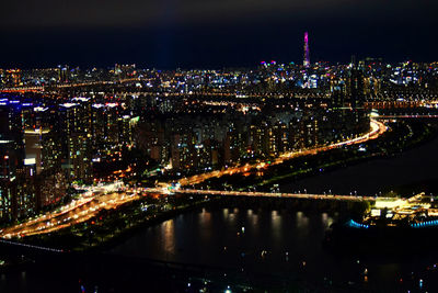 Illuminated bridge over river by buildings in city at night